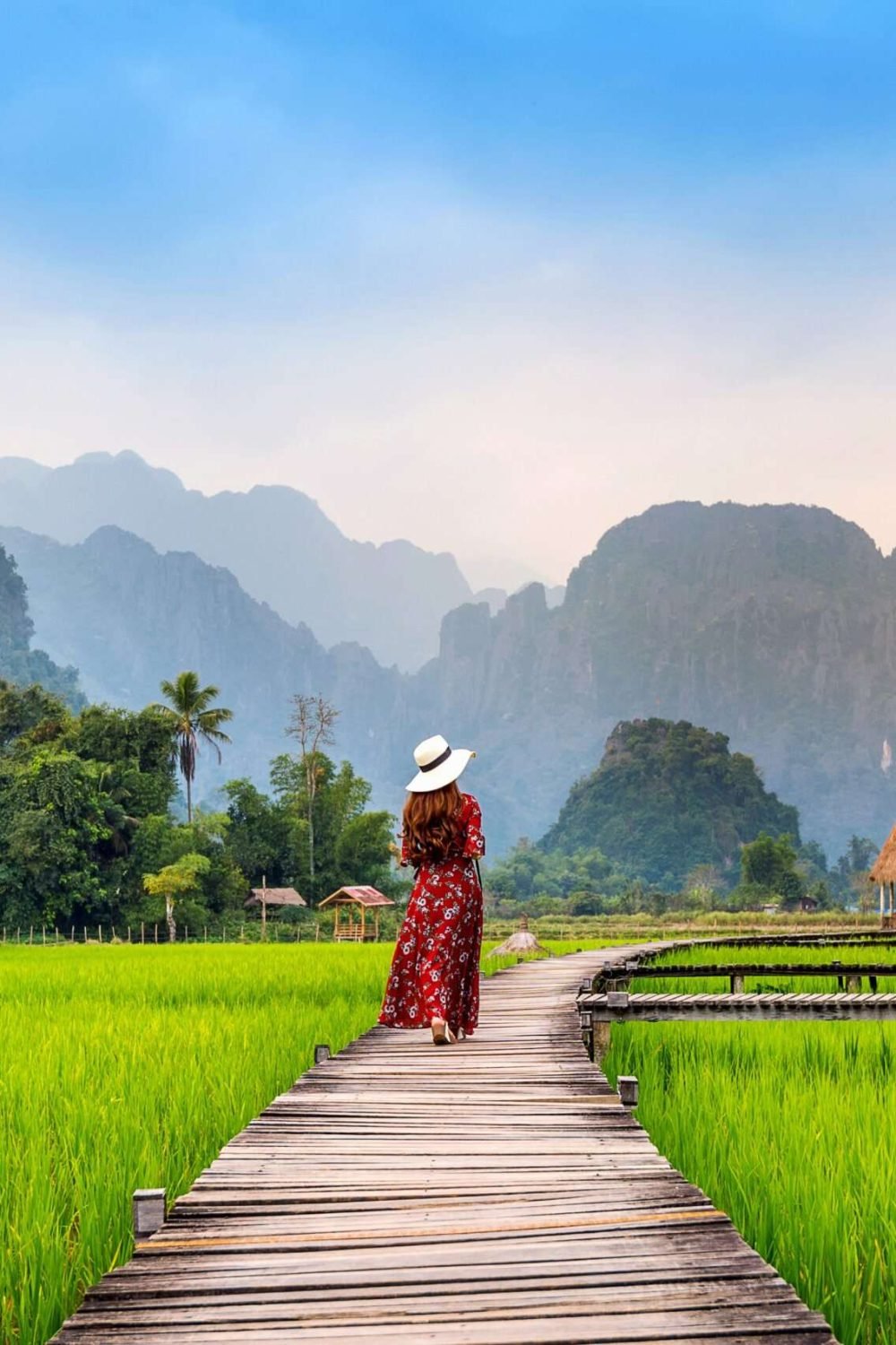 Young woman walking on wooden path with green rice field in Kerala